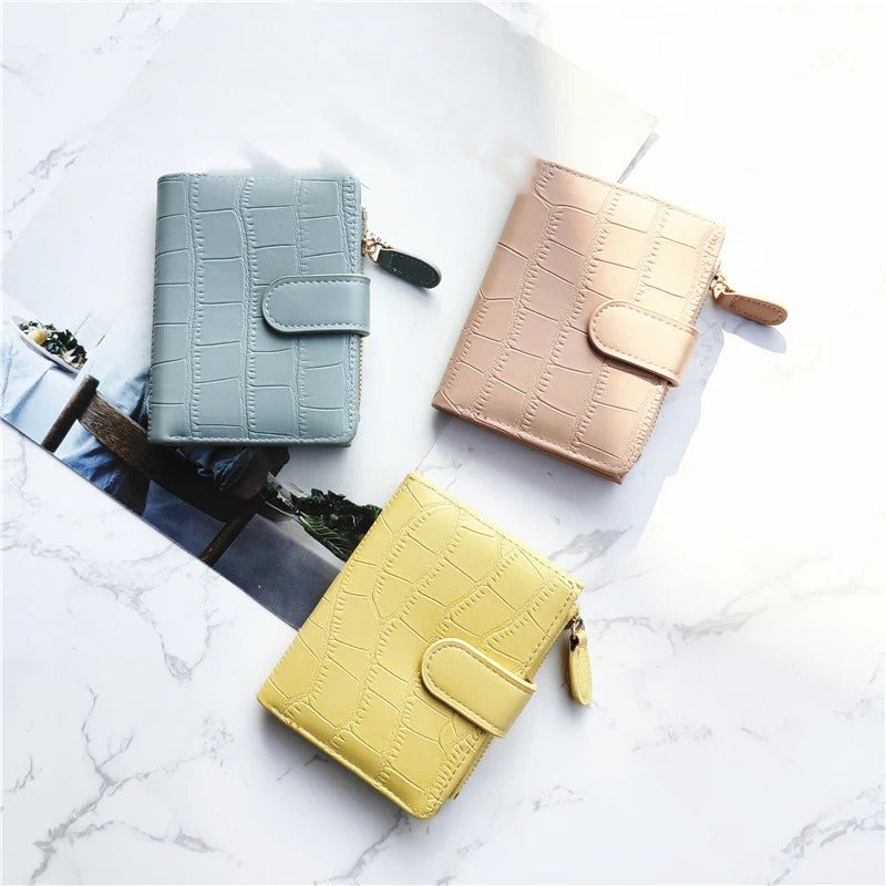 Compact zip wallet in dusty blue, blush pink and pale yellow, laid on a marble surface
